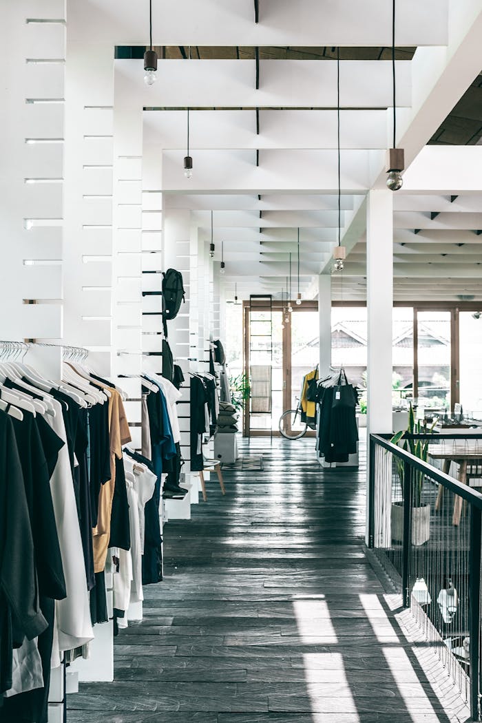 Interior of spacious modern fashion boutique with collection of various clothes hanging on racks in sunlight